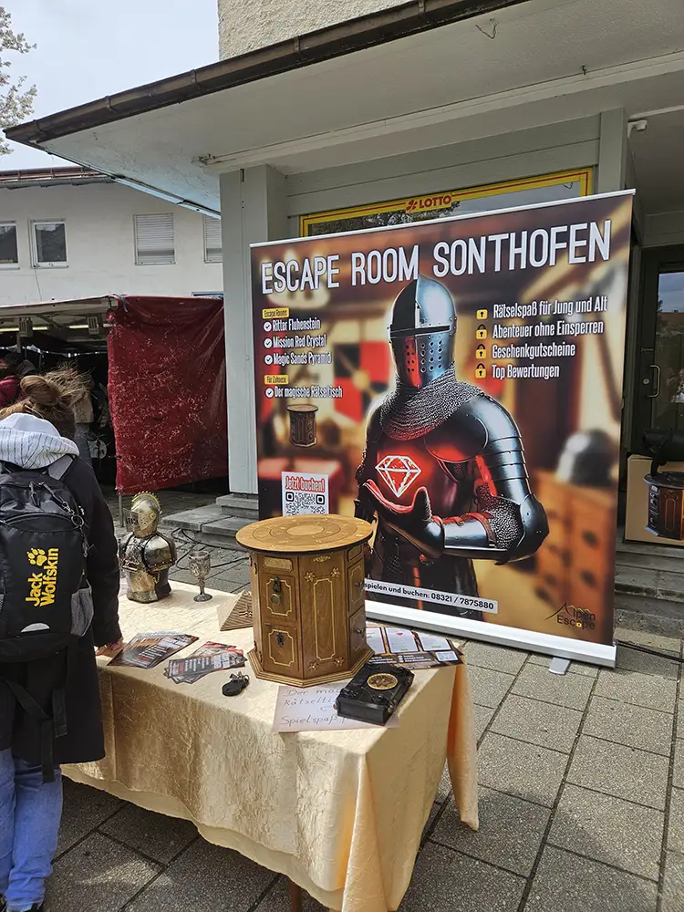Stand des Escape Room Sonthofen in der Fußgängerzone mit einem Werbebanner und ein paar Rätseln aus Holz.